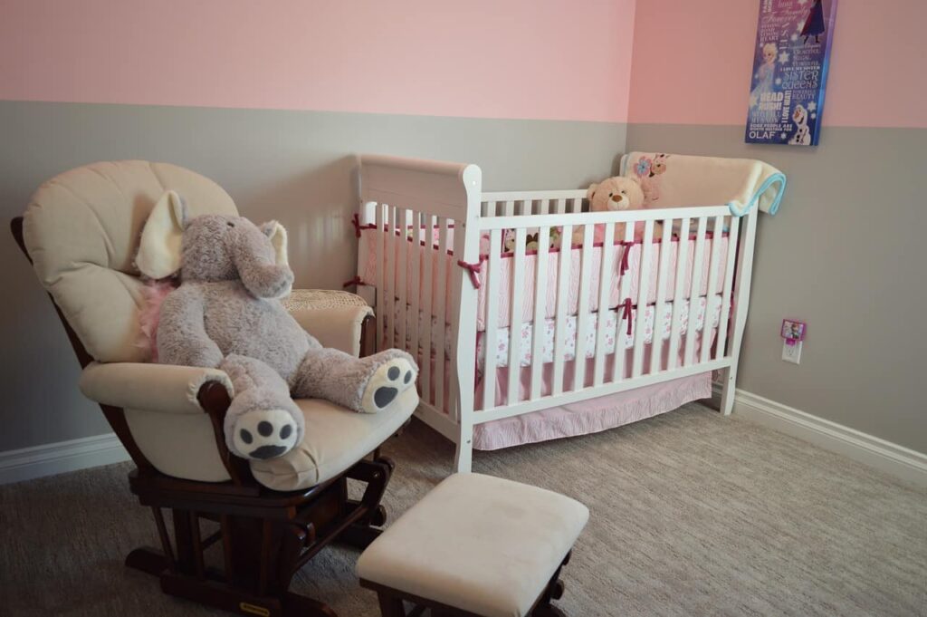 Cheap nursery glider with an elephant teddy sitting on it, and a white baby cot with a teddy in it